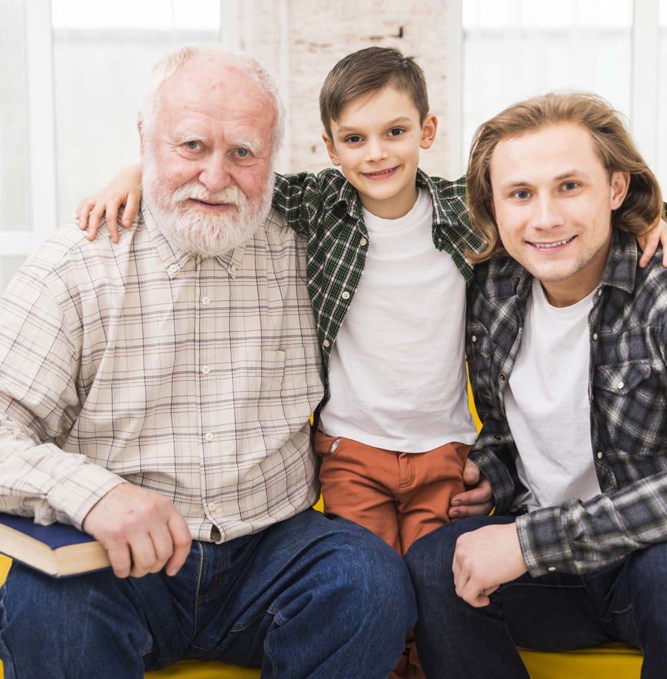 Vater, Enkel und Sohn sitzen nebeneinander. Der Enkel legt seite Arme auf die Schultern der Großvaters und des Vaters.